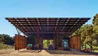 Award winning LSX Solar Panel Structure covering equipment barn with tractors parked inside and trees and vineyards in background