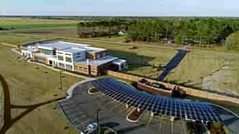 Aerial view of Solar Carport using custom LSX Solar panels built over parking lot surrounded by grass with two cars parked and Marlboro Electric Coop building in background in South Carolina