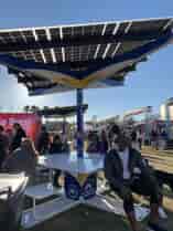 Solarzone Recharge Station with people sitting on benches under solar shade and charging phone devices.