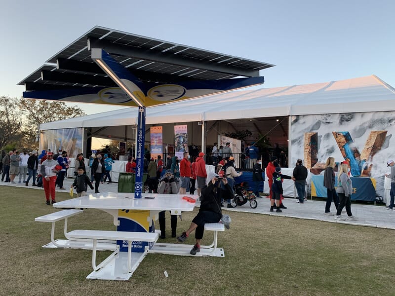 Solar Table on lawn in front of Super Bowl LV Experience provides shade, lighting, charging and comfortable seating for guests.