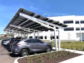 SolarScape Solar Carport with sideview of solar panels, covering parking spaces with cars parked in front of white office building