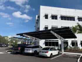 SolarScape Solar Carport covering parking spaces with cars parked and with office building in background with blue sky