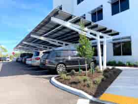 SolarScape Solar Carport covering parking spaces with cars parked in front of white office building